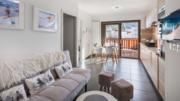 A modern living room with a sofa, a dining area, and a kitchen. There are framed pictures on the wall, and a balcony with a view of the snowy landscape. - Modern, cosy 4-person flat - close to the centre and skiing (Châtel)