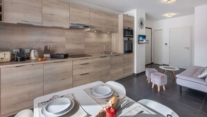 A modern kitchen with wooden cabinets, a built-in oven, and a dining area with a table set for two. - Modern, cosy 4-person flat - close to the centre and skiing (Châtel)