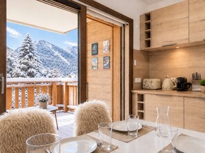 A dining area with a view of snow-covered mountains, wooden furniture, and kitchen appliances.