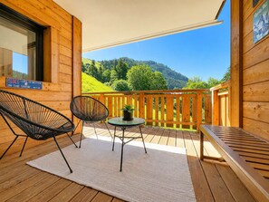 A wooden balcony with a table and chairs, a view of green hills, and a sign that says 'SKI LIFE IS BETTER IN THE SNOW'.