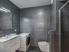 Ein modernes Badezimmer mit Waschmaschine, Toilette und einem großen Spiegel.