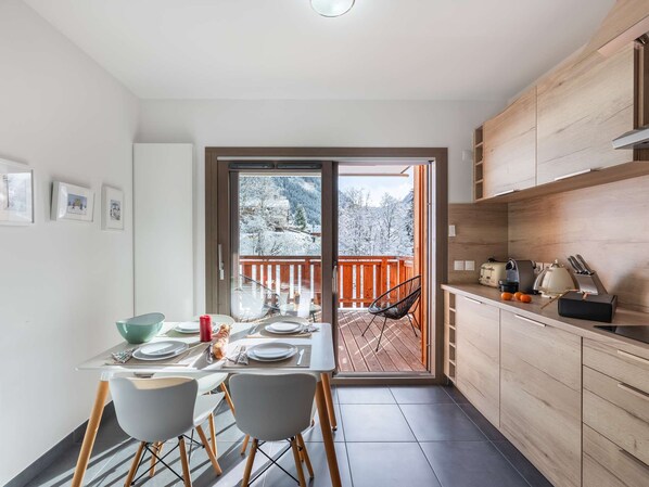 Eine moderne Küche mit Holzschränken, ein Essbereich mit Tisch für Zwei und Blick auf eine verschneite Terrasse.