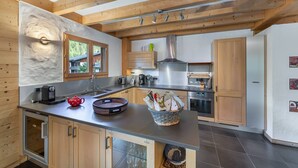 A modern kitchen with wooden beams, a large island, and stainless steel appliances. - Chalet 10 pers - large spaces, fireplace, quiet location (Châtel)