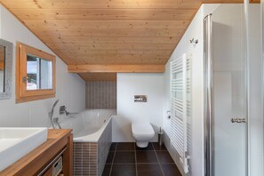 A modern bathroom with a wooden ceiling, a bathtub, a toilet, and a shower area.