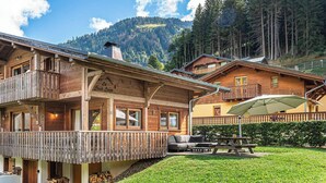 A wooden chalet with balconies, a patio area, and a mountain backdrop. - Chalet 10 pers - large spaces, fireplace, quiet location (Châtel)