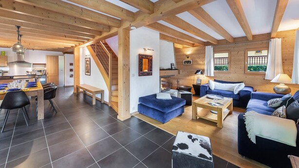 A spacious living area with a wooden ceiling, a dining area with a table and chairs, and a staircase leading to another level. - Chalet 10 pers - large spaces, fireplace, quiet location (Châtel)
