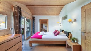 A bedroom with a wooden bed, a wooden dresser, a bedside table, and a view through a glass door to an outdoor deck. - Chalet 10 pers - large spaces, fireplace, quiet location (Châtel)