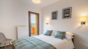 Ein Hotelzimmer mit Bett, Stuhl, einer zur Balkontür führenden Tür und zwei Wandleuchten.