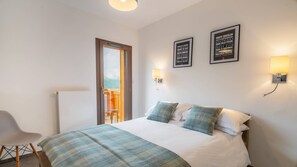 A hotel room with a bed, a chair, a door leading to a balcony, and two wall-mounted light fixtures.