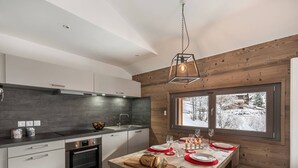 Eine moderne Küche mit Holzvertäfelung, einem für zwei Personen gedecktem Esstisch und einem Fenster mit Blick auf Schnee.