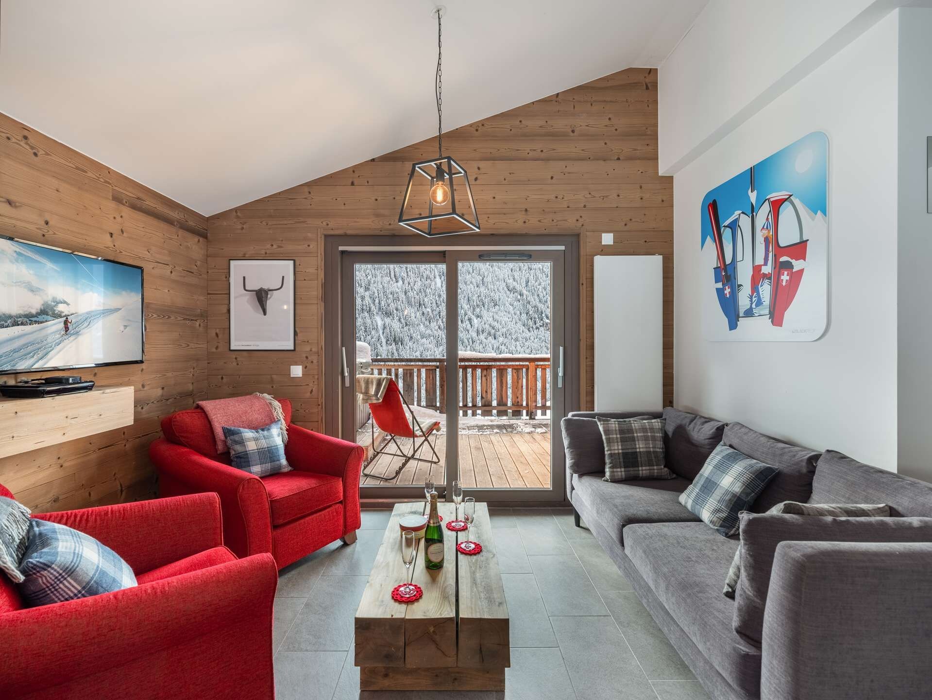 Una sala de estar acogedora con detalles de madera, un sofá rojo, un sofá gris y una mesa de centro de madera con una botella y vasos.