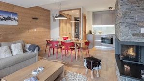A modern living room with a fireplace, a dining area with red chairs, and a kitchen with stone accents. - 4-person flat - fireplace, close to the centre and slopes (Châtel)