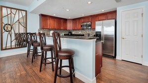 A kitchen with wooden cabinets, a stainless steel refrigerator, and a bar stool area.