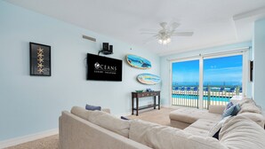 A living room with a large beige sectional sofa, a ceiling fan, and a TV displaying "OCEANS LUXURY VACATIONS".