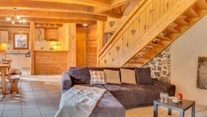 A cozy log cabin interior with a sofa, a dining area, and a staircase with heart-shaped cutouts. - 8-person flat in adjoining chalet, village centre, close to slopes (LA CHAPELLE D ABONDANCE)