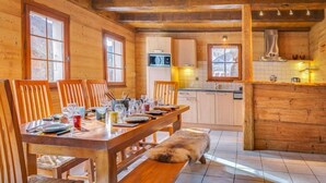 A wooden interior with a dining table set for four, a kitchen area, and a large window. - 8-person flat in adjoining chalet, village centre, close to slopes (LA CHAPELLE D ABONDANCE)