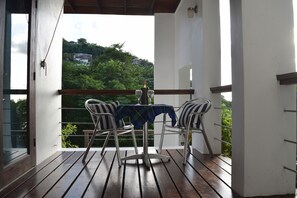 A balcony with a table and chairs, a bottle of wine, and a view of a hillside. - The White Turtle Villa  ~ Marigot Bay, private pool, water views. (Marigot Bay)