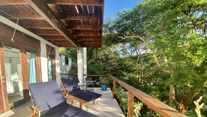 Eine Holzterrasse mit zwei Liegestühlen und einem Tisch, umgeben von üppigem Grün und einem Holzgeländer.
