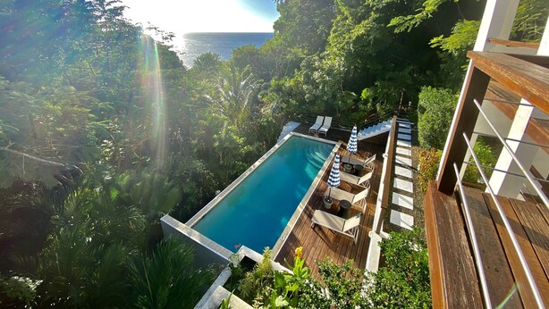 Ein Poolbereich mit Holzterrasse, Liegestühlen und Sonnenschirmen.