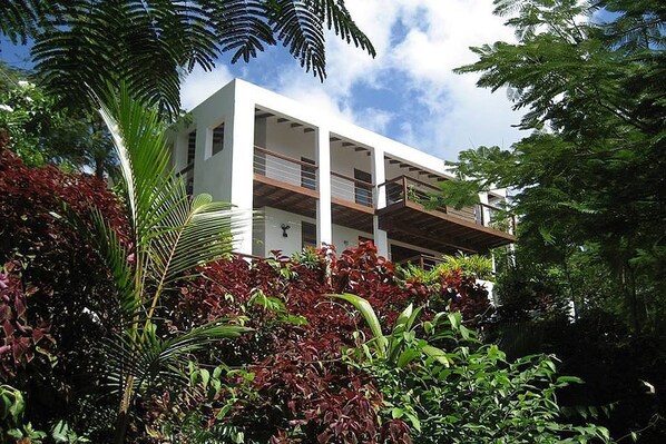 A modern multi-story building with balconies, surrounded by lush tropical vegetation. - The White Turtle Villa  ~ Marigot Bay, private pool, water views. (Marigot Bay)