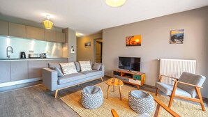 Ein modernes Wohnzimmer mit einem grauen Sofa, einem Flachbildfernseher und einem Couchtisch aus Holz.