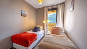 Ein kleines Schlafzimmer mit zwei Betten, einem Fenster mit Vorhängen, einem Bild an der Wand und einer Lampe.