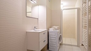 Ein modernes Badezimmer mit Waschbecken, Spiegel, integriertem Waschmaschinenanschluss und Duschkabine aus Glas.