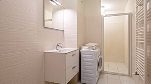 A modern bathroom with a white sink, a mirror, a built-in washing machine, and a glass shower enclosure.