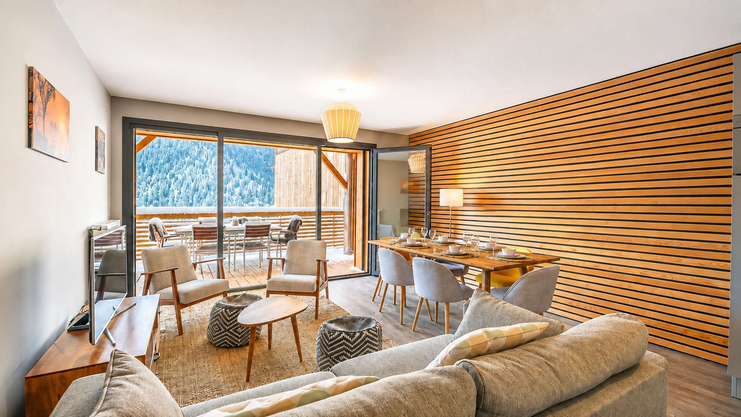 Un salon moderne avec un canapé, des fauteuils, une table à manger et une vue sur un paysage enneigé, visible à travers de grandes fenêtres.