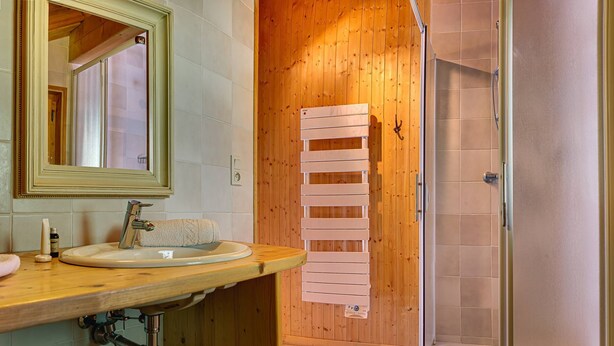 Une salle de bain avec un meuble-lavabo en bois, un miroir, une serviette et un espace douche.