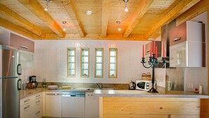 A modern kitchen with wooden beams, a central island, stainless steel appliances, and a view of the outdoors through windows. - Chalet 7 people - authentic chalet, close to the village (Châtel)
