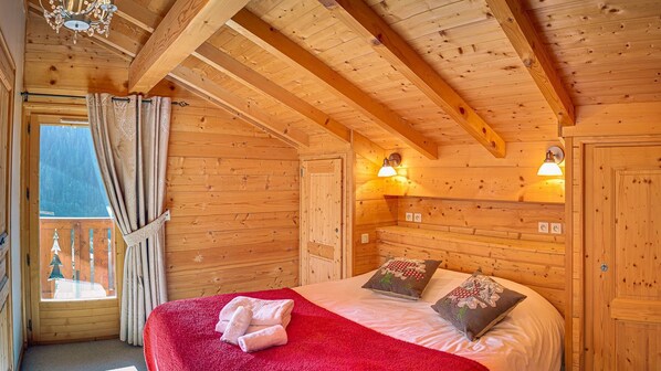 A wooden cabin bedroom with a bed, two wall-mounted lamps, and a window with curtains. - Chalet 7 people - authentic chalet, close to the village (Châtel)