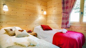 A cozy cabin room with two beds, wooden walls, and a window with curtains. - Chalet 7 people - authentic chalet, close to the village (Châtel)