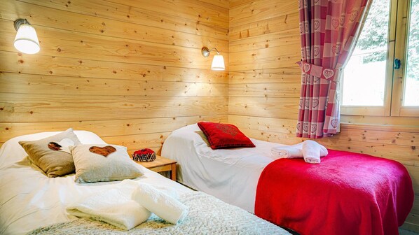 A cozy cabin room with two beds, wooden walls, and a window with curtains. - Chalet 7 people - authentic chalet, close to the village (Châtel)