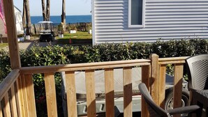 Eine Holzterrasse mit Blick auf ein weißes Wohnmobil und das Meer.