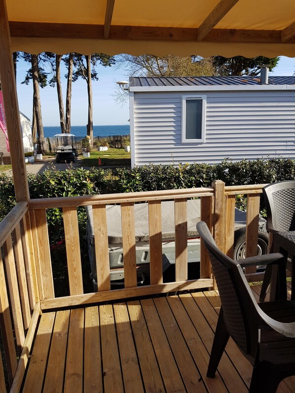 A wooden deck with a view of a white mobile home and the ocean.