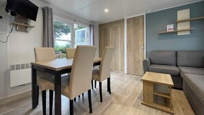 Ein modernes Wohnzimmer mit Essbereich, einem grauen Sofa, einem kleinen Holztisch und einem an der Wand befestigten Fernseher.