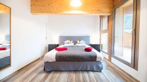 Una habitación de hotel moderna con una cama grande, techo de madera y ventanas amplias.