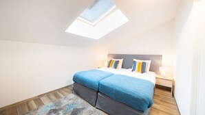 Un dormitorio con tragaluz, una cama con ropa de cama azul, una mesita de noche y una alfombra.