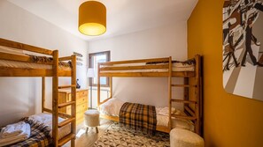 A dormitory room with bunk beds, a small desk, a lamp, and a geometric patterned rug.