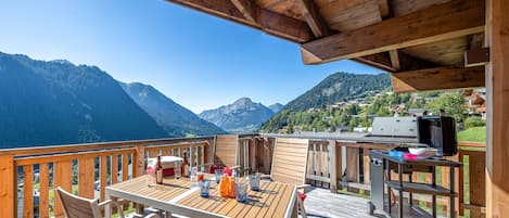 Una terraza de madera con mesa y sillas, con vista a un paisaje montañoso.