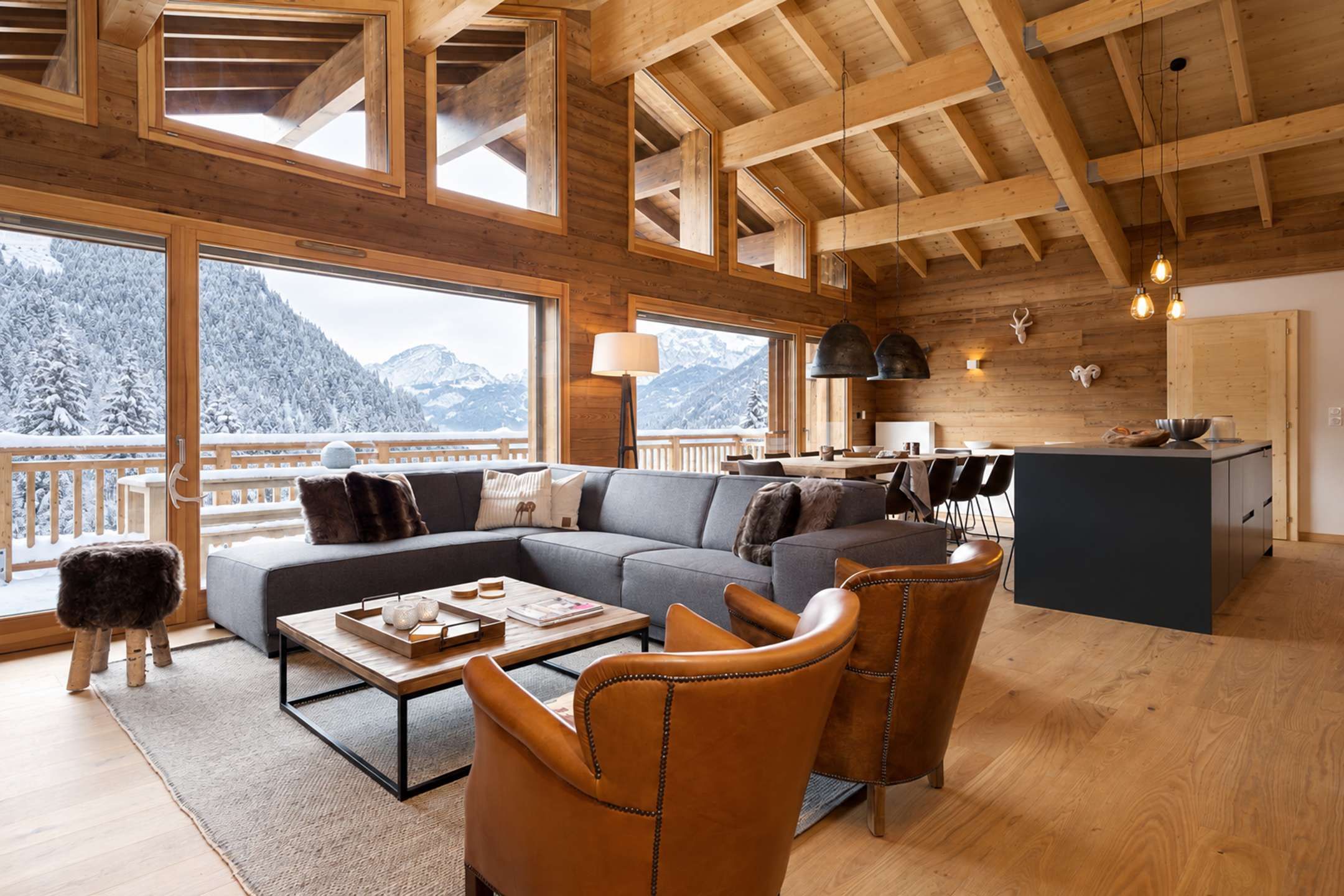 Un vaste espace de vie comprenant un grand canapé, des fauteuils en cuir, une table basse et une vue sur des montagnes enneigées, grâce à de grandes fenêtres.