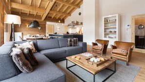 Ein modernes Wohnzimmer mit Holzboden, einem grauen Ecksofa, einem Ledersessel und einem Couchtisch.