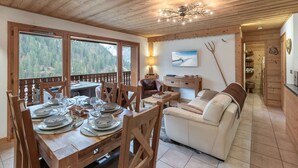 Comedor con piso de madera, una mesa dispuesta para seis personas, un sofá y un televisor en una esquina.