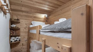 Una pequeña habitación estilo cabaña con literas, repisas con peluches y un taburete de madera.