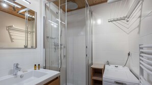 Un baño moderno con ducha de vidrio, un lavabo blanco con gabinete de madera y una secadora Whirlpool.