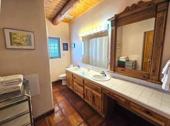 Un baño con armarios de madera, lavamanos doble, un espejo grande con luces y un perchero para toallas.