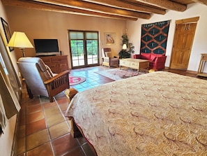 Ein Schlafzimmer mit einem großen Bett, einem Holzstuhl, einem Fernseher und einer Tür, die auf einen Balkon führt.