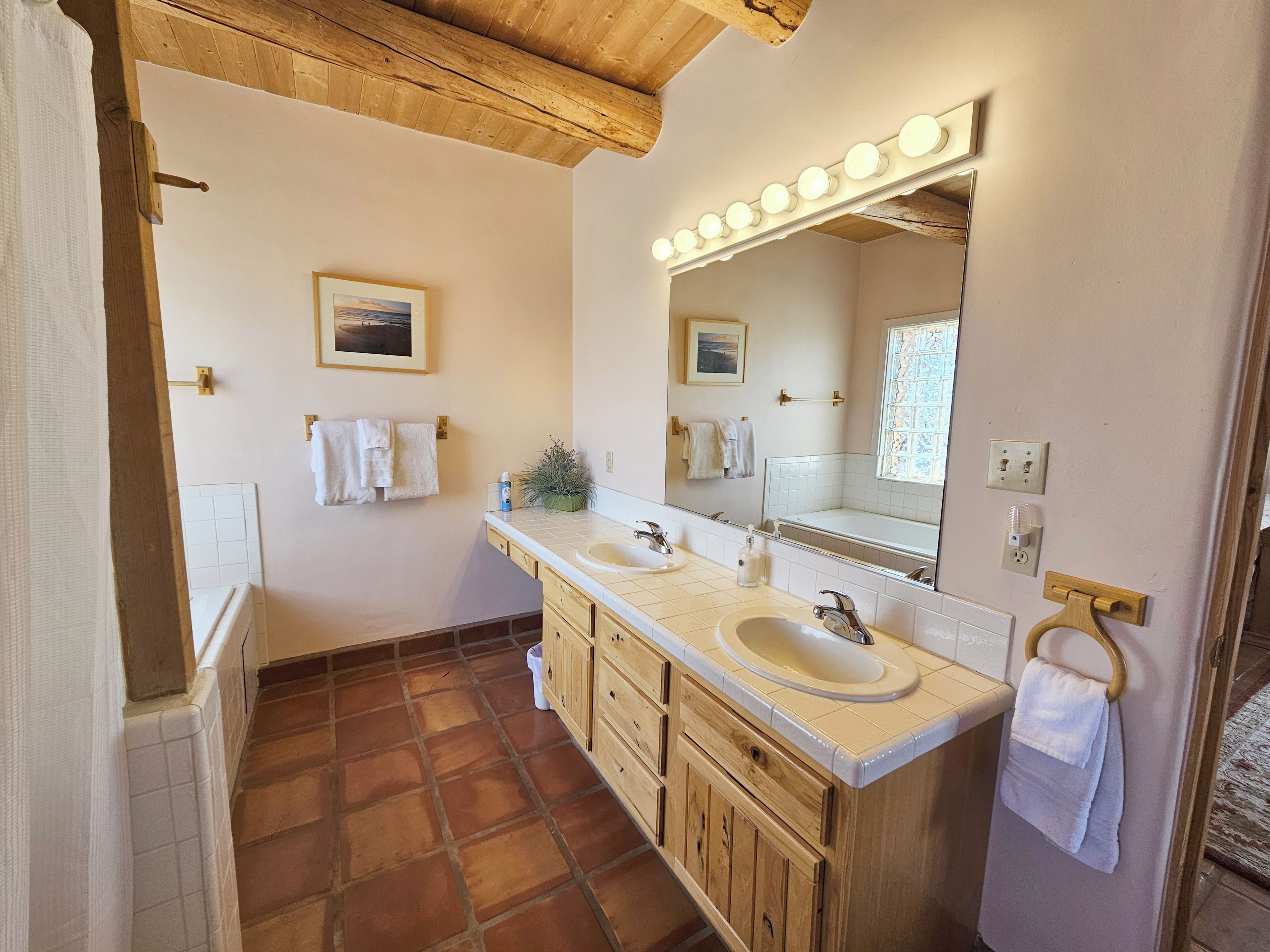 A bathroom with two sinks, wooden cabinets, a large mirror with lights, and a tiled floor.