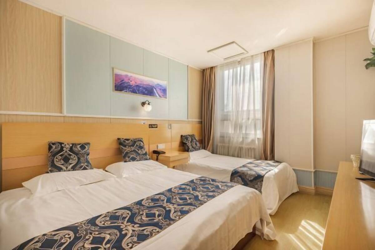 A hotel room with two beds, a desk, a TV, and a painting on the wall.